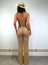 Load image into Gallery viewer, Back view of a model wearing luxury gold crochet trousers and a straw hat, showcasing a beach-ready look.