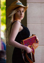Load image into Gallery viewer, Woman holding a handmade honey leather Carriel bag with vibrant Mola applique, wearing a stylish hat.