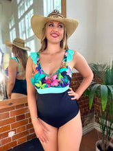 Charger l'image dans la galerie, Model wearing Bahia tummy control swimsuit in floral design with black bottom, accessorized with a wide-brimmed hat.