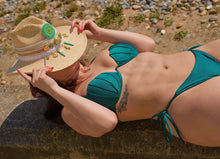 Load image into Gallery viewer, Woman lounging in a teal bikini and straw hat, enjoying a sunny beach day.