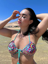Load image into Gallery viewer, Model wearing the Madeiria hand-beaded ruched bikini on the beach, showcasing vibrant patterns and luxurious fabrics.