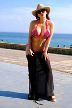 Load image into Gallery viewer, Model wearing the Catriona hand beaded bikini in fuchsia with a black cover-up and hat, standing by the ocean.
