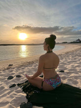 Load image into Gallery viewer, Woman in handcrafted hand-beaded bikini meditating on the beach at sunset, showcasing vibrant patterns and luxury fabrics.