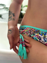 Load image into Gallery viewer, Close-up of a hand holding the tassel of a handcrafted beaded bikini, showcasing vibrant colors and intricate detailing.
