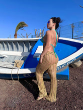 Load image into Gallery viewer, Woman modeling luxury crochet trousers by a colorful boat under a sunny sky.