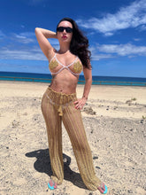 Load image into Gallery viewer, Model showcasing luxury crochet trousers in gold on a beach, perfect for summer cover-ups.