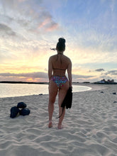 Load image into Gallery viewer, Model wearing the Madeira hand beaded ruched bikini, standing on sandy beach during sunset.