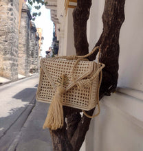 Load image into Gallery viewer, Handwoven Iraca palm leaf shoulder bag displayed on a tree, showcasing its artisanal design and natural materials.
