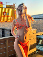 Load image into Gallery viewer, Model showcases Delilah hand-beaded orange bikini by the beach, highlighting its elegance and intricate beadwork.