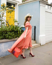 Load image into Gallery viewer, Woman in a burnt orange dress and straw hat, walking with a vibrant handbag near a blue wall.
