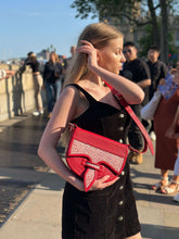 Load image into Gallery viewer, Woman in a black dress holding a red Handmade Rubi Leather Carriel Bag with Mola on a city street.