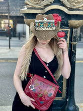 Load image into Gallery viewer, Woman with a handmade, hand-painted red leather handbag and a decorative straw hat, outdoors, showcasing stylish accessories.