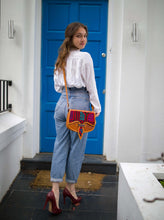Load image into Gallery viewer, Model showcasing handmade Honey Leather Carriel bag with Mola applique in front of a blue door.