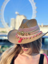 Load image into Gallery viewer, Handmade Iraca Palm Hat adorned with colorful accents, worn by a woman against a scenic background.