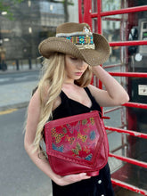 Load image into Gallery viewer, Model wearing a hand-painted red Tala Leather Handbag, styled with a straw hat in an urban setting.
