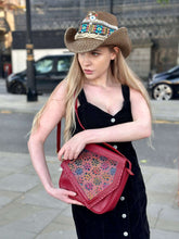 Load image into Gallery viewer, Woman in a stylish hat holding a red handmade Tala Leather handbag with intricate patterns.