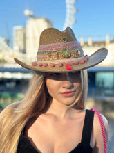 Load image into Gallery viewer, Handmade Iraca Palm Hat with colorful embroidery and embellishments, worn by a model in a sunny outdoor setting.