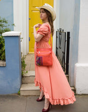 Load image into Gallery viewer, Model wearing a burnt orange leather handbag and pink ruffled dress, standing in front of a yellow door.