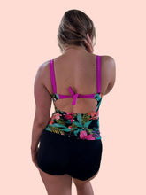 Load image into Gallery viewer, Back view of a woman wearing a vibrant floral tankini with pink straps and black shorts.