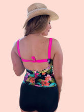 Load image into Gallery viewer, Woman in a floral tankini with a bow clasp on the back, wearing black shorts and a straw hat.