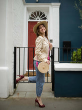 Load image into Gallery viewer, Woman wearing a beige jacket and hat, holding a handmade Iraca palm canteen bag, standing outside a stylish home.