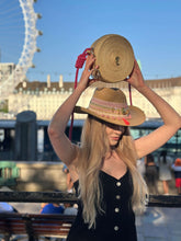 Load image into Gallery viewer, Model showcasing a handmade Iraca palm canteen bag and a straw hat against a scenic backdrop.