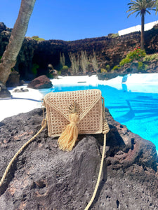 Handwoven Iraca palm leaf shoulder bag with tassel detail, placed on a rocky surface by a blue swimming pool.