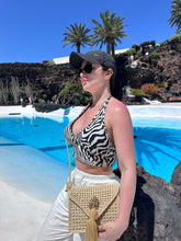 Load image into Gallery viewer, Woman in zebra print top by pool holding a handwoven Iraca palm leaf shoulder bag.