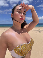 Cargar imagen en el visor de la galería, Woman in hand-beaded Nina bikini with gold embellishments, posing on a beach under sunny skies.