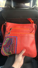 Load image into Gallery viewer, Handcrafted Burnt Orange Leather Handbag with Mola displayed in a car, showcasing unique MOLA embroidery and zippered compartments.