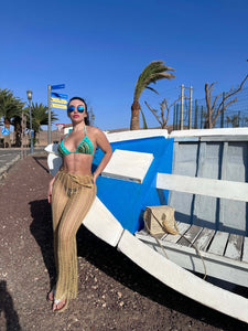 Woman in bikini and sunglasses next to a colorful boat, enjoying a sunny day at the beach.